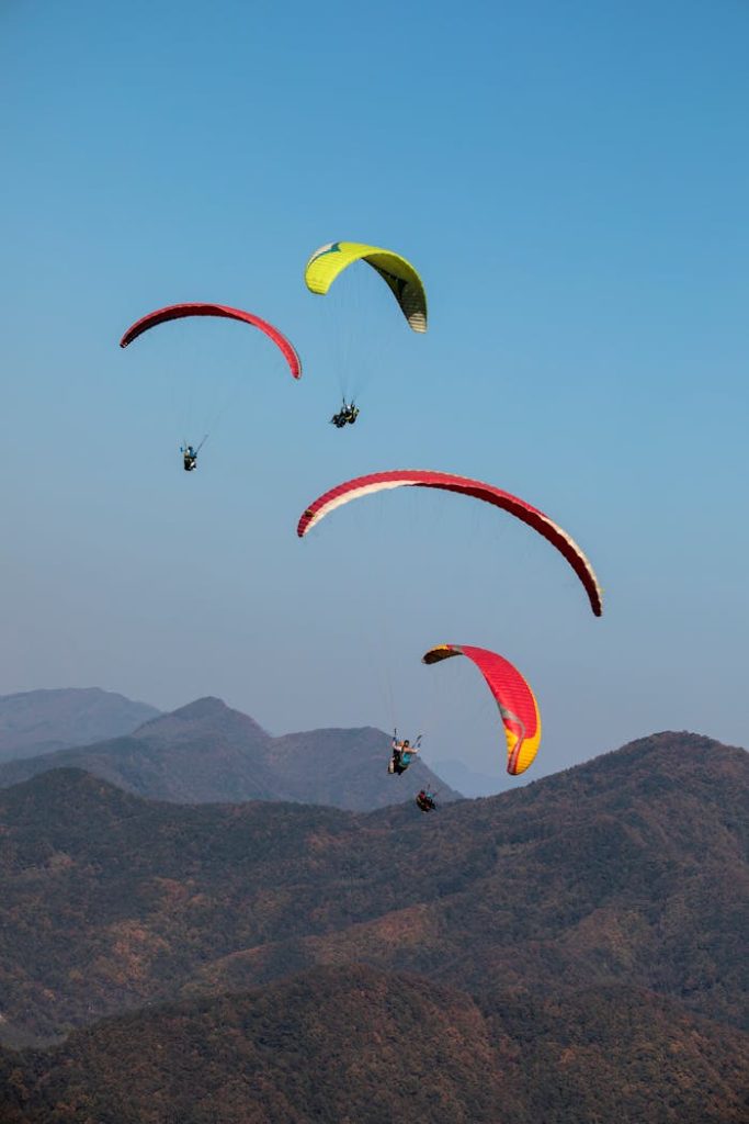 Colorful paragliders soar over scenic mountains in Danyang. Perfect for adventure seekers.