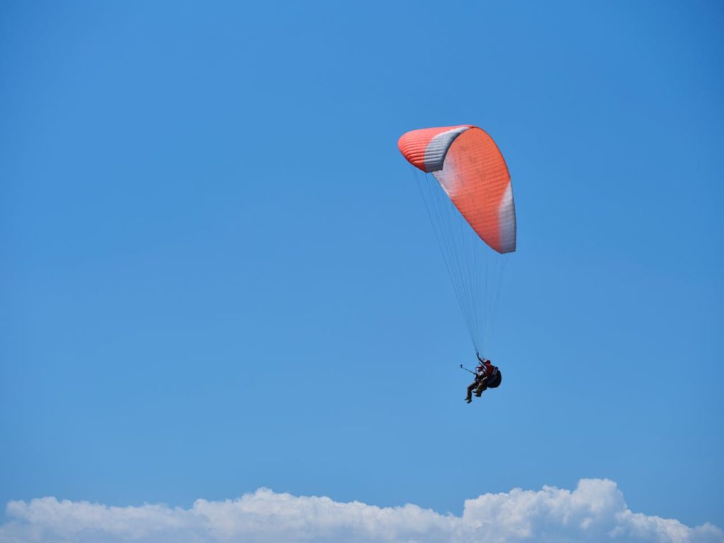 Paraglider soaring gracefully with a vibrant red parachute against a blue sky backdrop.